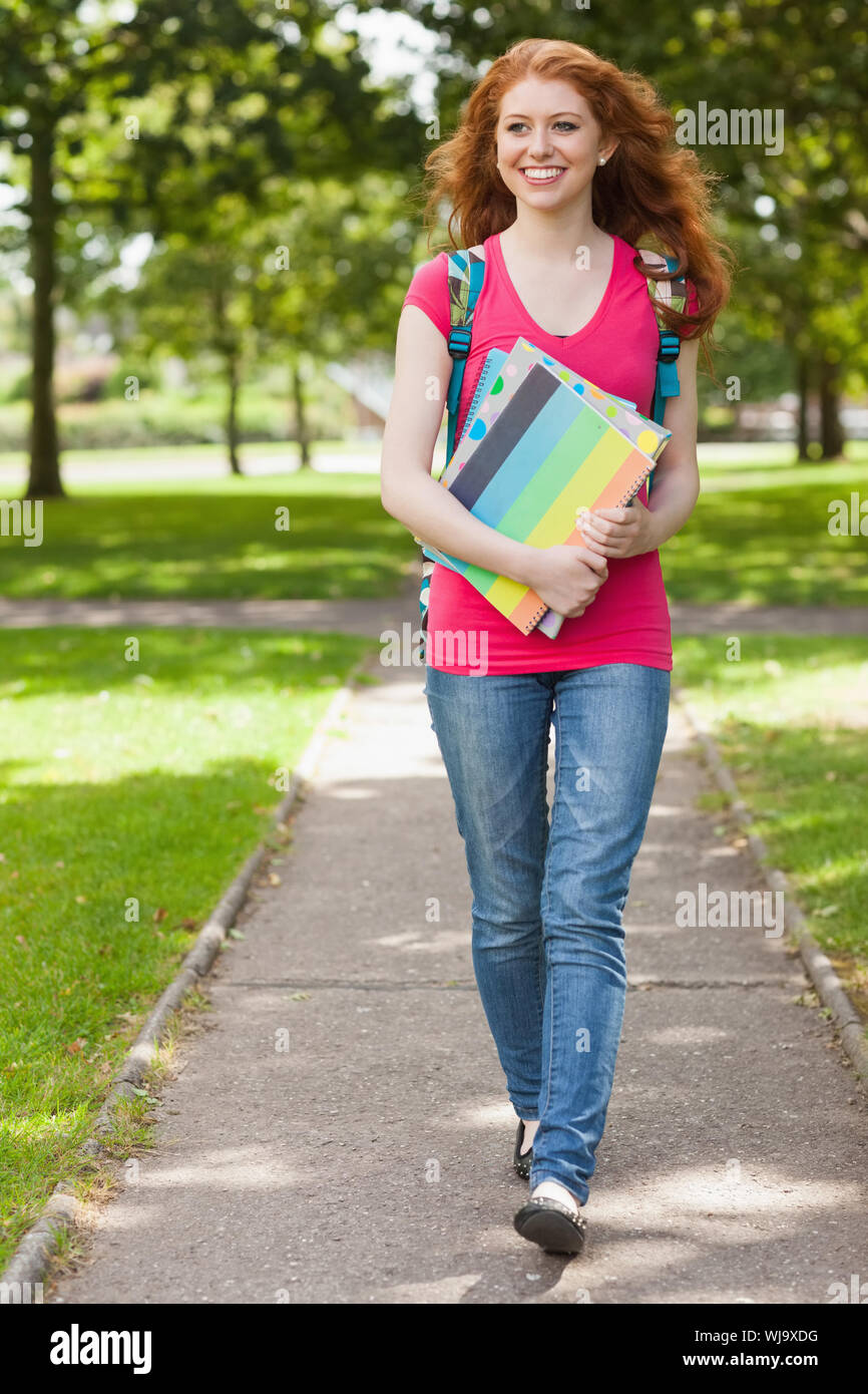 Gorgeous studente sorridente camminare e trasportare notebook sul campus presso il college Foto Stock