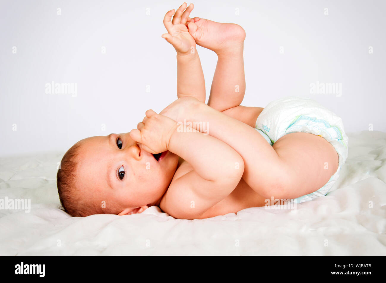 Piccolo bambino mangiare i suoi piedi sul letto Foto Stock