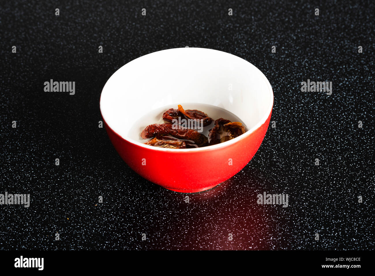 Recipiente rosso secco con tomatoe messo in acqua. Su sfondo nero. Foto Stock