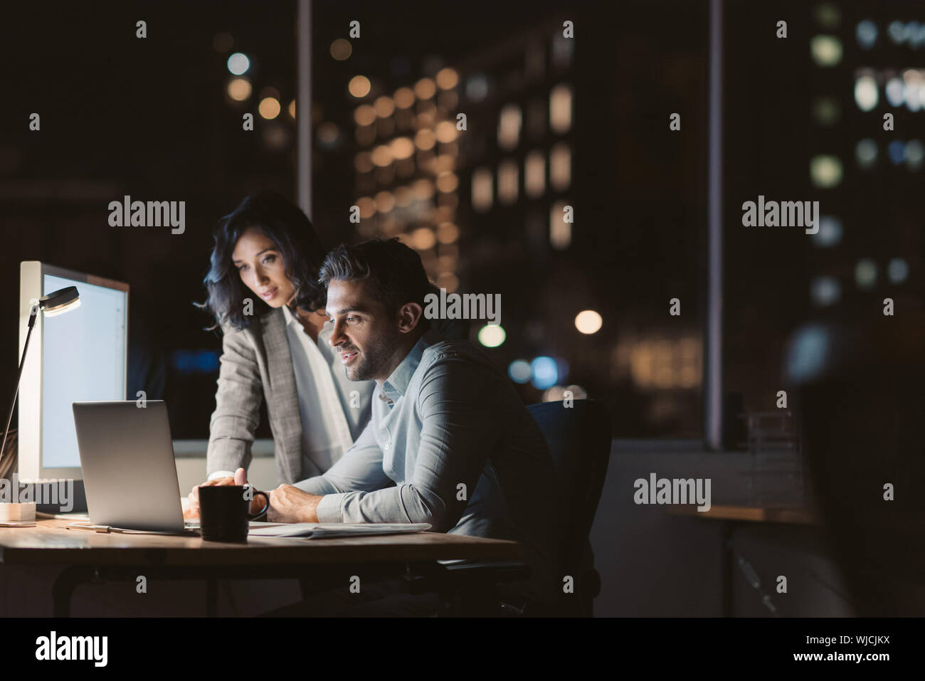 Due colleghi di lavoro mediante un computer portatile a tarda sera Foto Stock