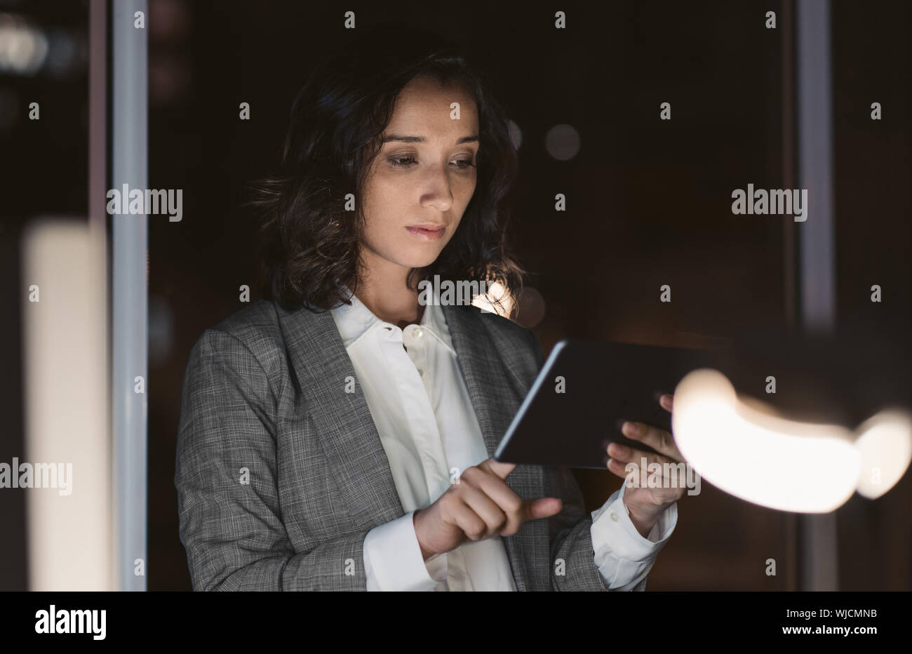 Giovane imprenditrice utilizzando il suo tablet in un ufficio scuro Foto Stock