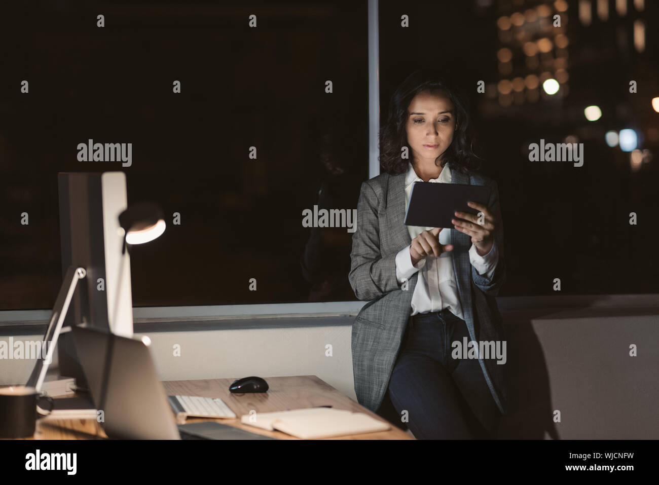 Giovane imprenditrice in piedi in un buio office utilizzando il suo tablet Foto Stock
