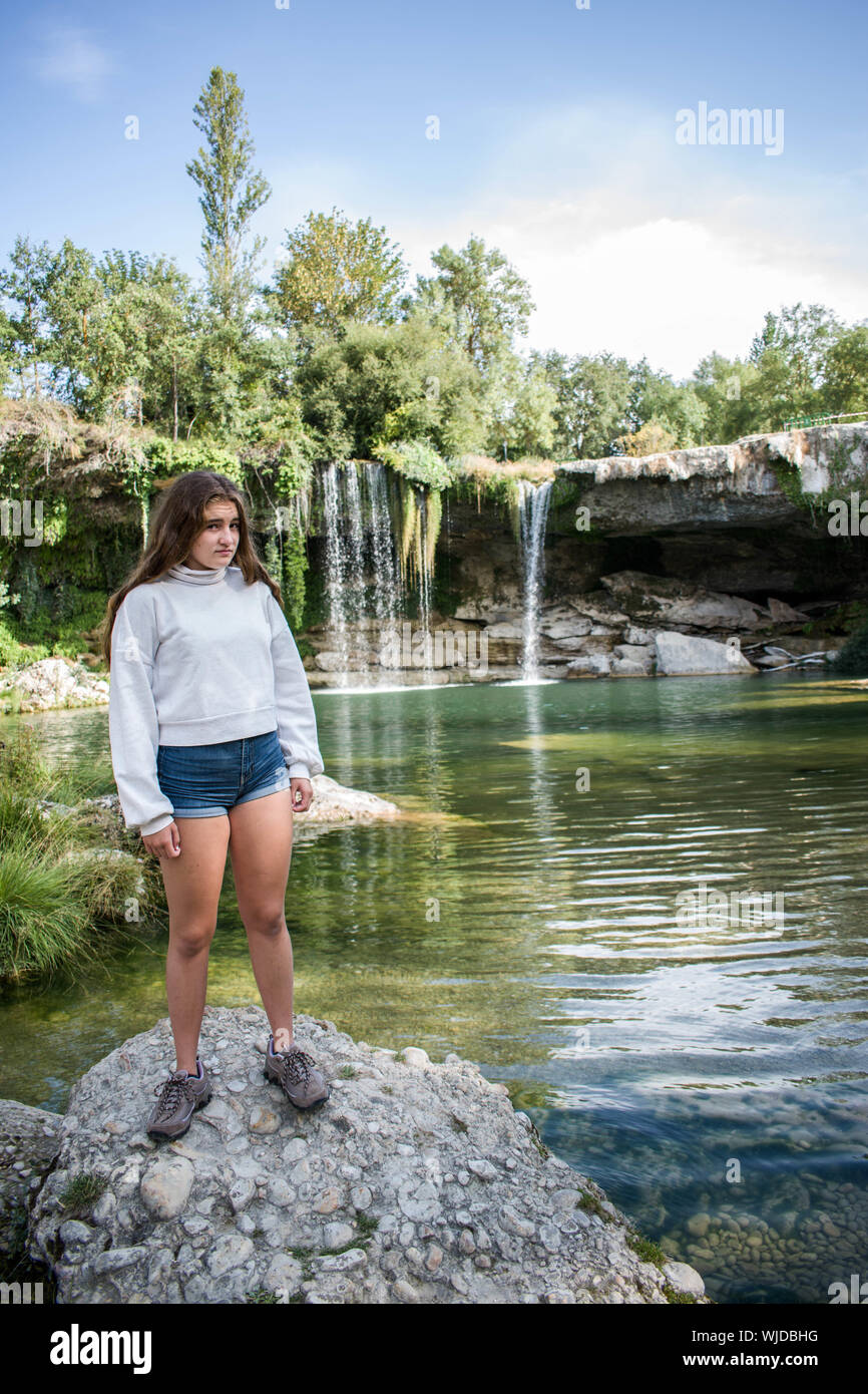 Rilassata piuttosto giovane ragazza in posa di un lago con cascata Foto Stock