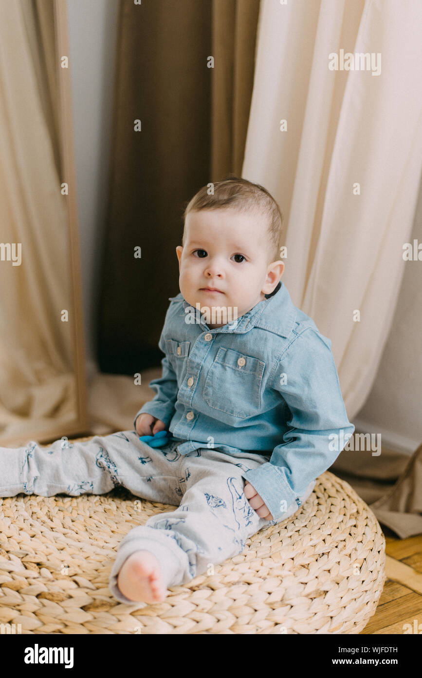 Bambino di un anno in una camicia denim siede su un puff beige. Un bambino in un dolce impostazione Foto Stock