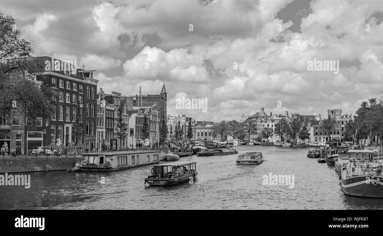 Un canale di Amsterdam con le barche e gli edifici storici, in un giorno nuvoloso in bianco e nero, in Olanda, Amsterdam, Paesi Bassi Foto Stock