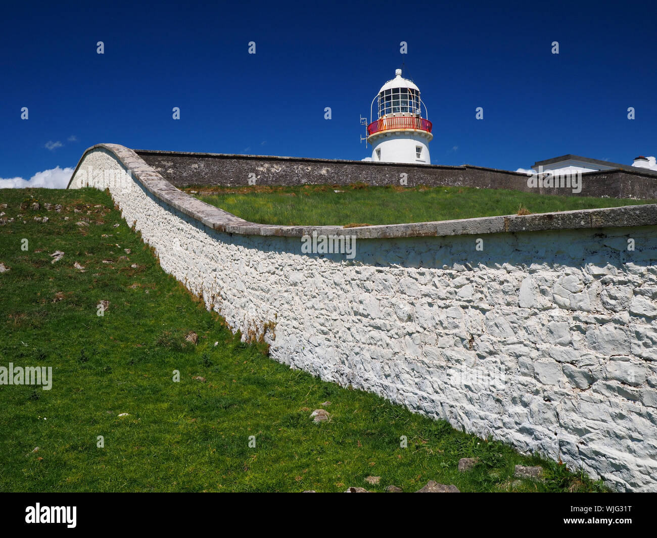 San Giovanni punto, Co. Donegal, Irlanda - 21 Maggio 2019 - faro bianco dietro bianco parete fieldstone davanti ad un cielo blu chiaro Foto Stock