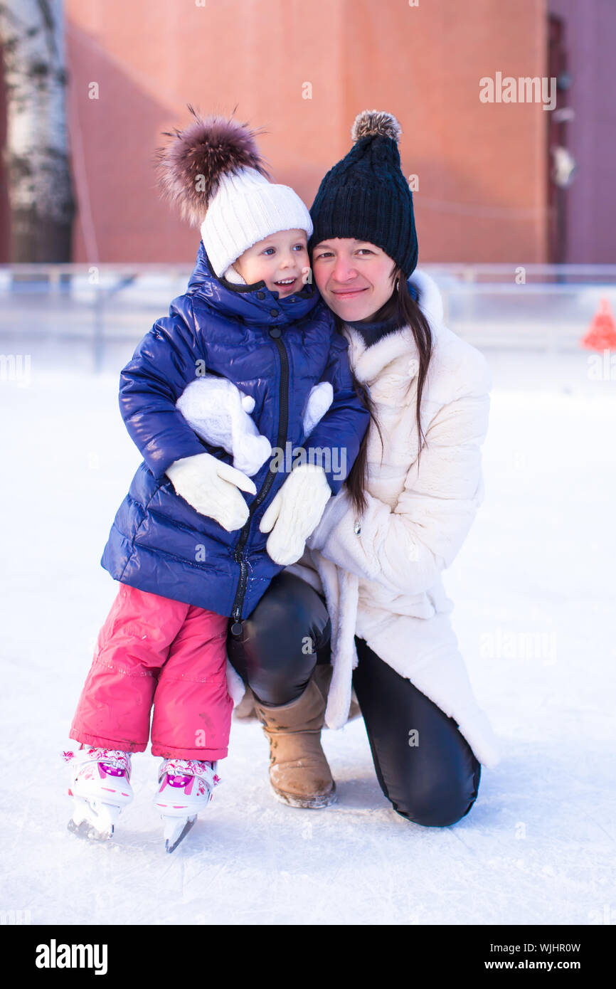 Sorridente giovane madre e la sua incantevole piccola figlia pattinaggio sul ghiaccio insieme Foto Stock