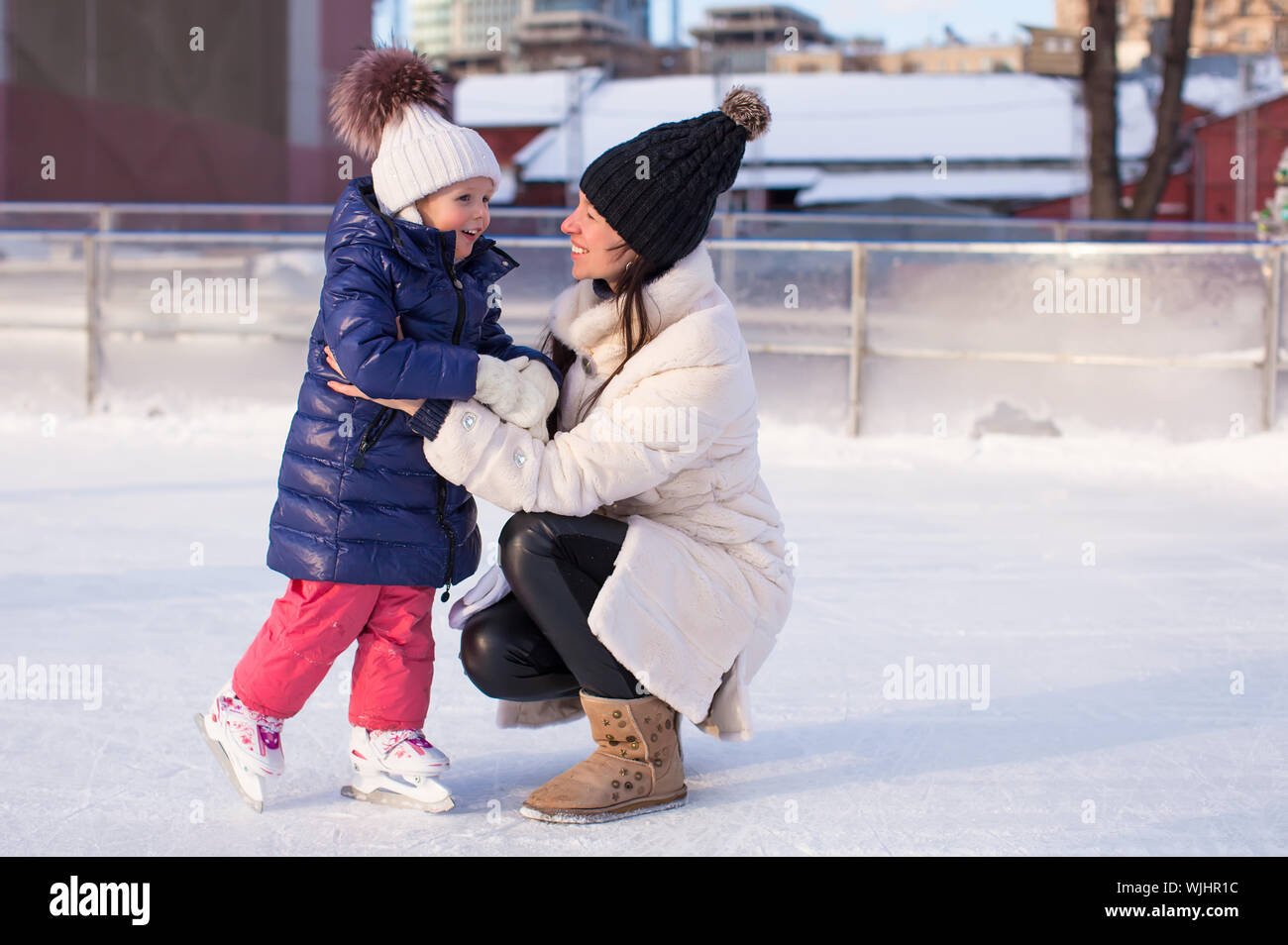 Sorridente giovane madre e la sua incantevole piccola figlia pattinaggio sul ghiaccio insieme Foto Stock