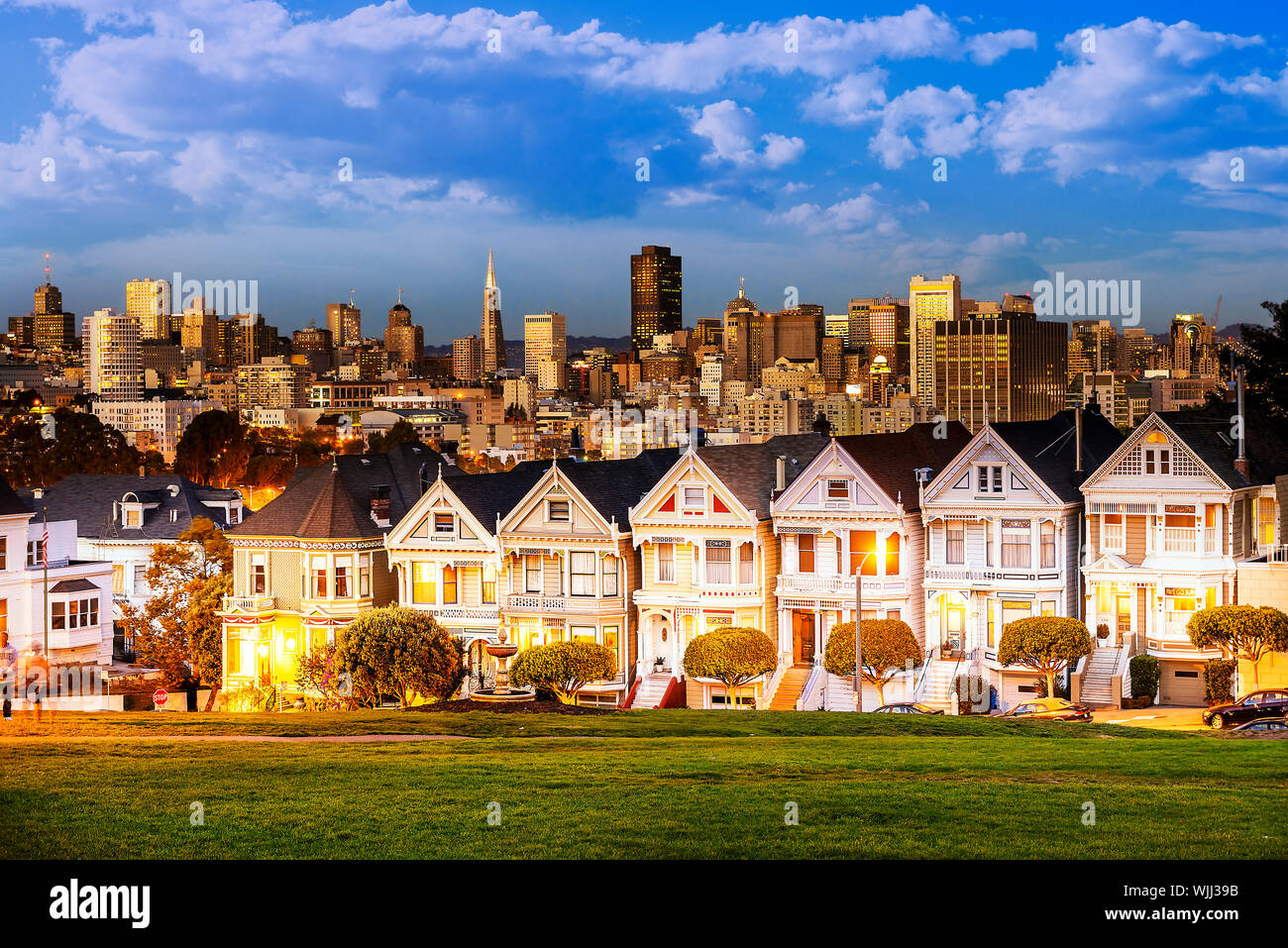 Il Painted Ladies di San Francisco, California sit incandescente in mezzo sullo sfondo di un tramonto e grattacieli. Foto Stock