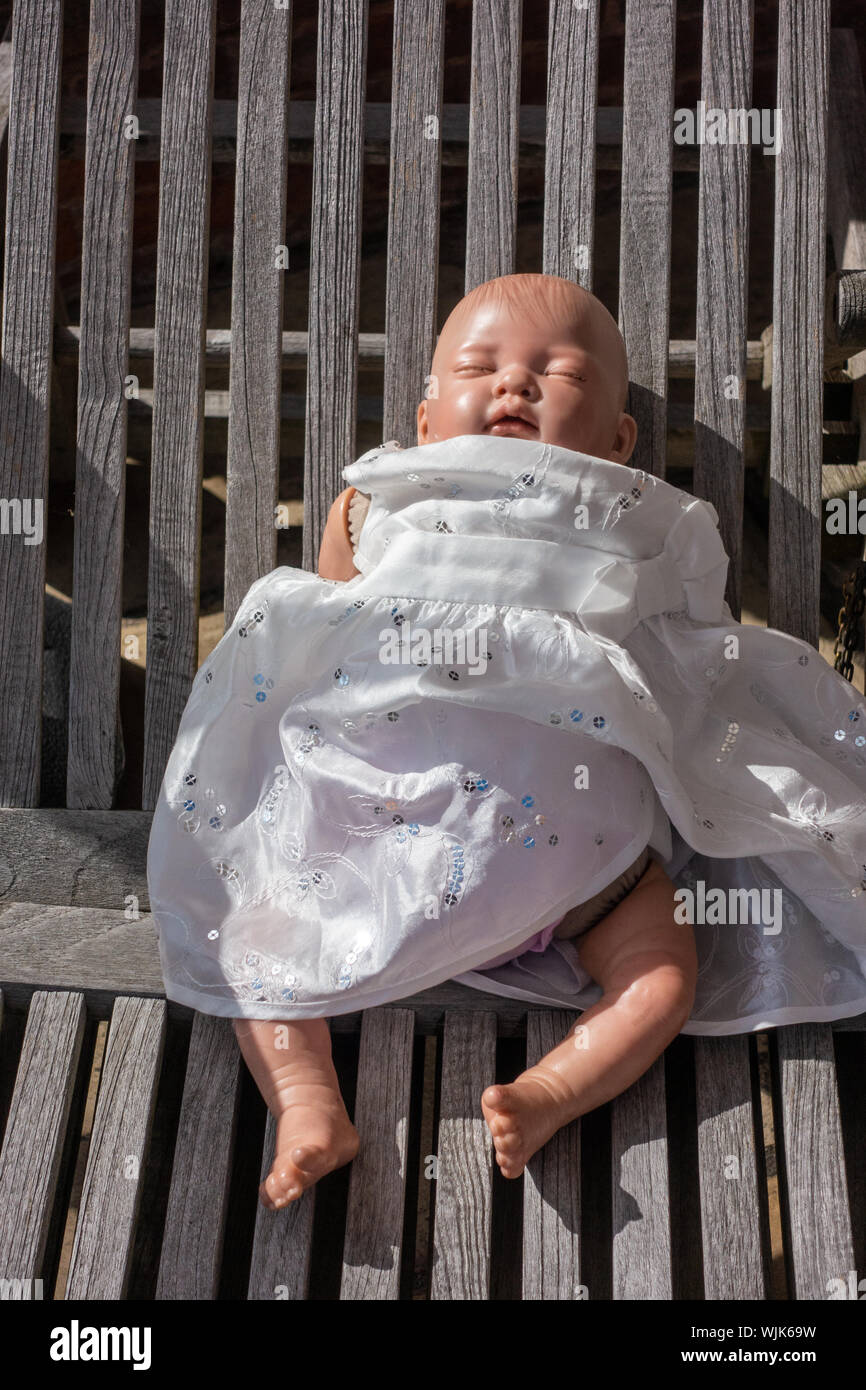 Piccoli baby doll giocattolo in un abito bianco e posa su una sedia da giardino Foto Stock