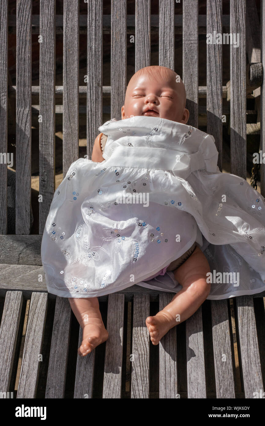 Piccoli baby doll giocattolo in un abito bianco e posa su una sedia da giardino Foto Stock