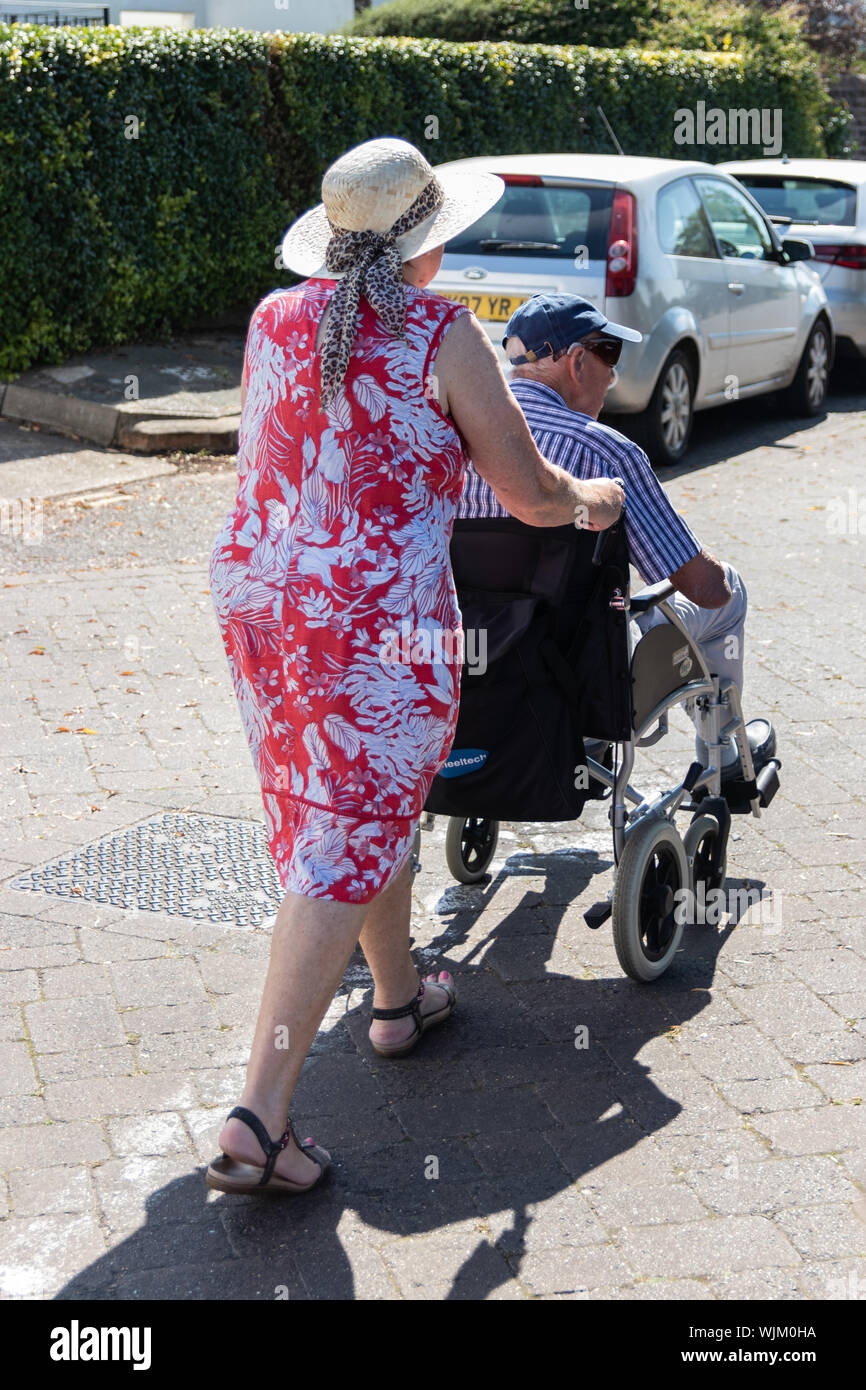 Una donna di mezza età spingendo un uomo anziano in una sedia a rotelle, i vecchi/persona disabile con accompagnatore Foto Stock