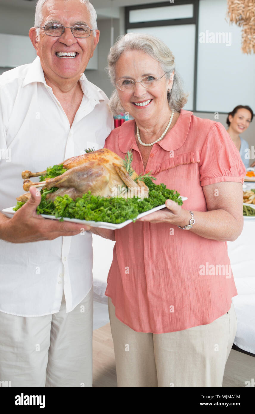 Ritratto di coppia senior tenendo il pollo arrosto in casa Foto Stock