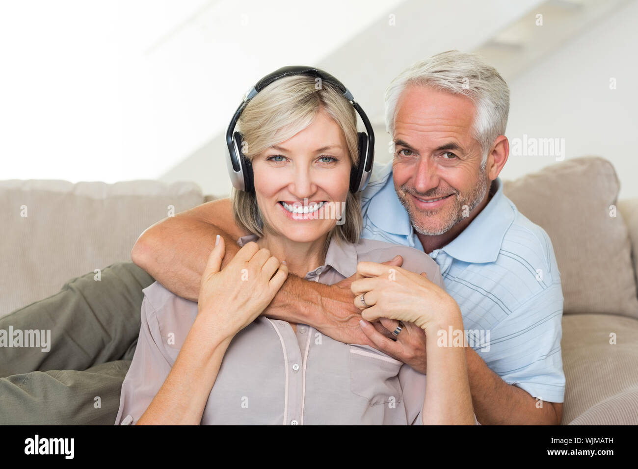 Sorridente uomo maturo abbracciando la donna da dietro sul divano di casa Foto Stock