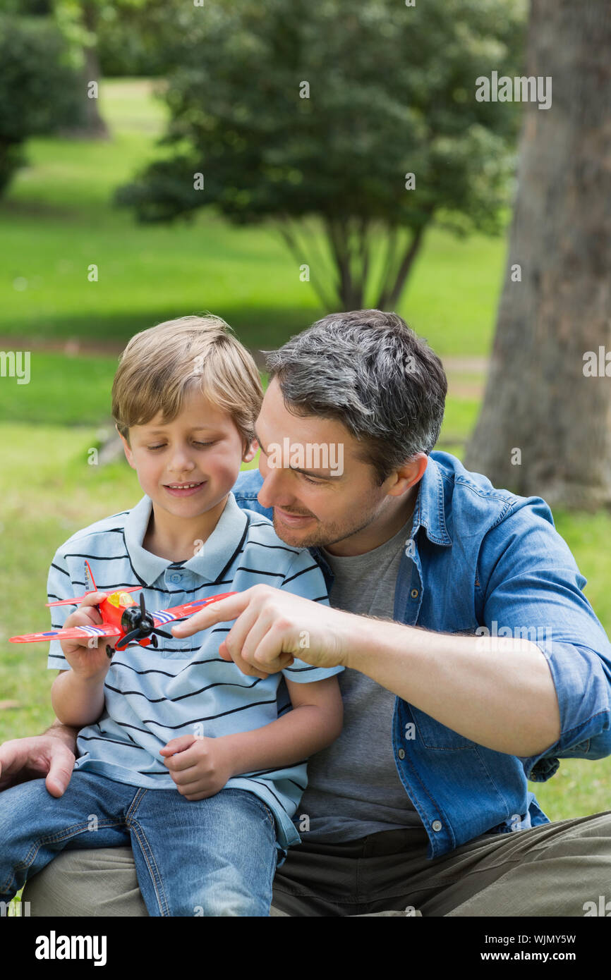 Ragazzo con aeroplano giocattolo seduto sul padre di giro al parco Foto Stock