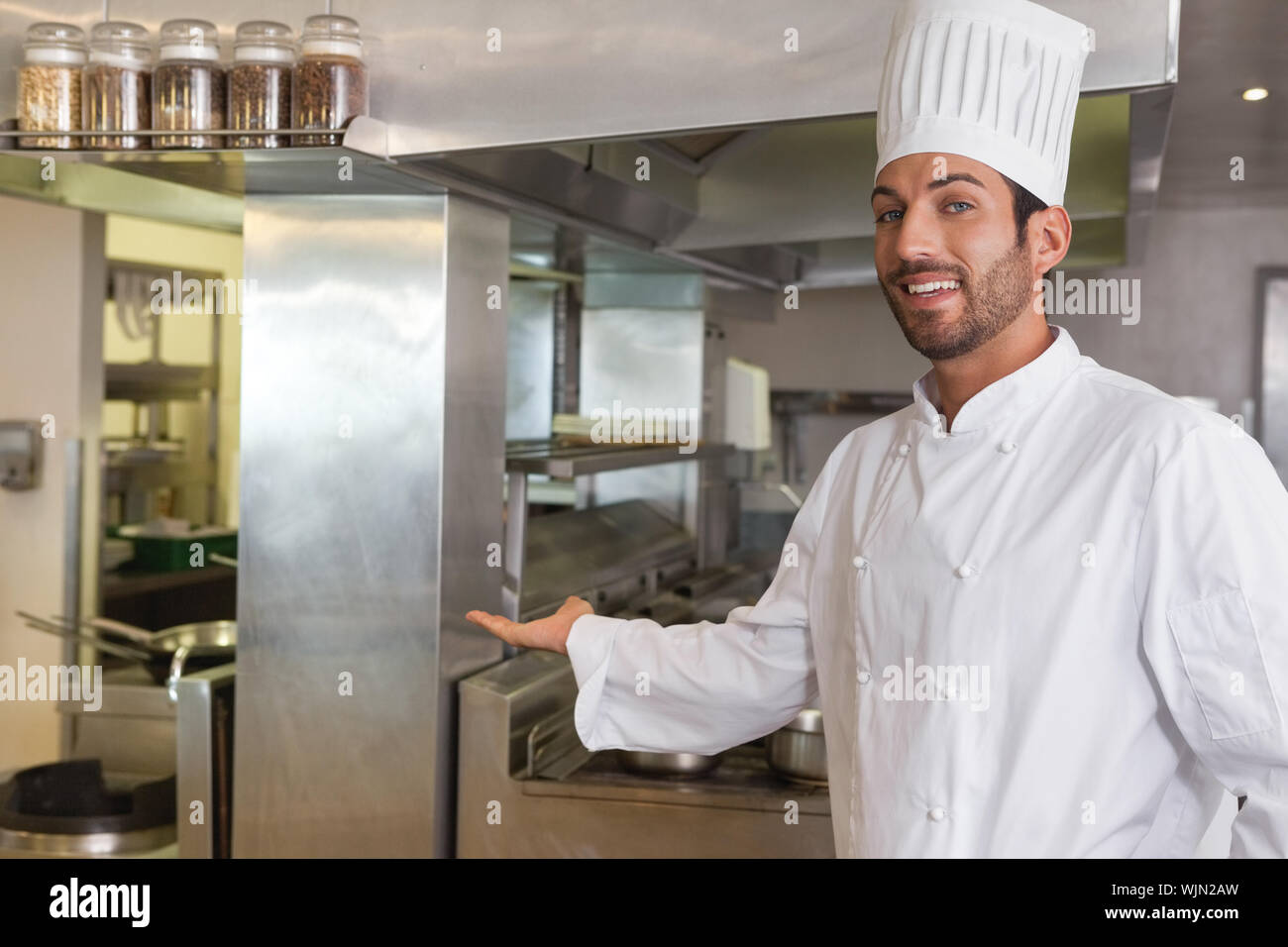 Sorridente giovane chef guardando la telecamera che mostra il suo luogo di  lavoro di una cucina commerciale Foto stock - Alamy