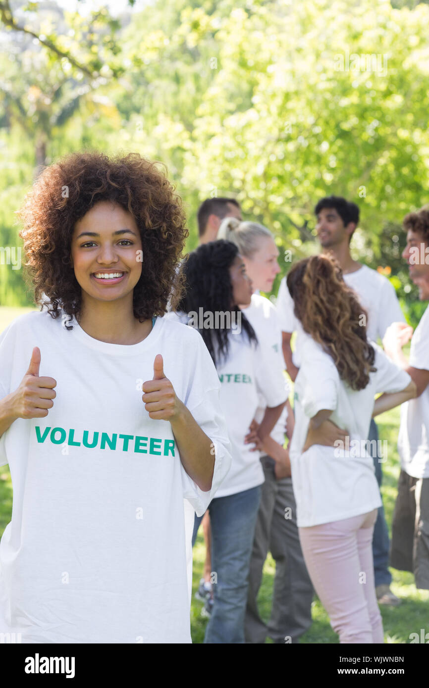 Fiducioso volontari femmina gesticolando Thumbs up con gli amici disucssing in background Foto Stock
