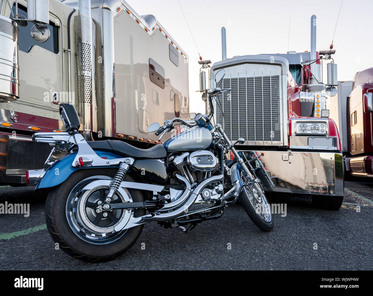 Classic motociclo come modo di trasporto alternativo e un hobby di un autista del camion durante il riposo è parcheggiato di fronte a una fila di big rig classic semi Foto Stock