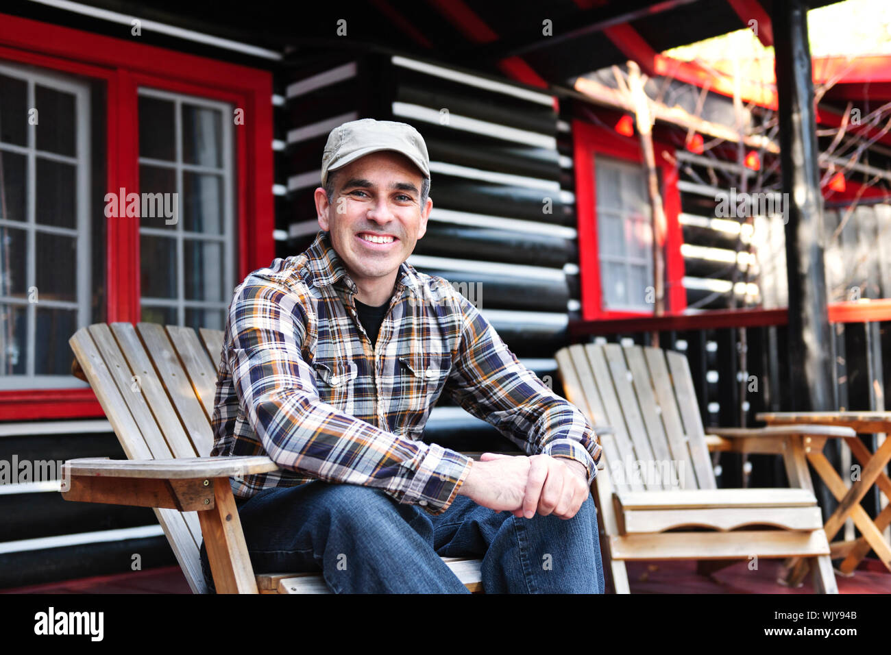 Uomo sorridente seduto sul ponte cottage in legno sedia adirondack Foto Stock