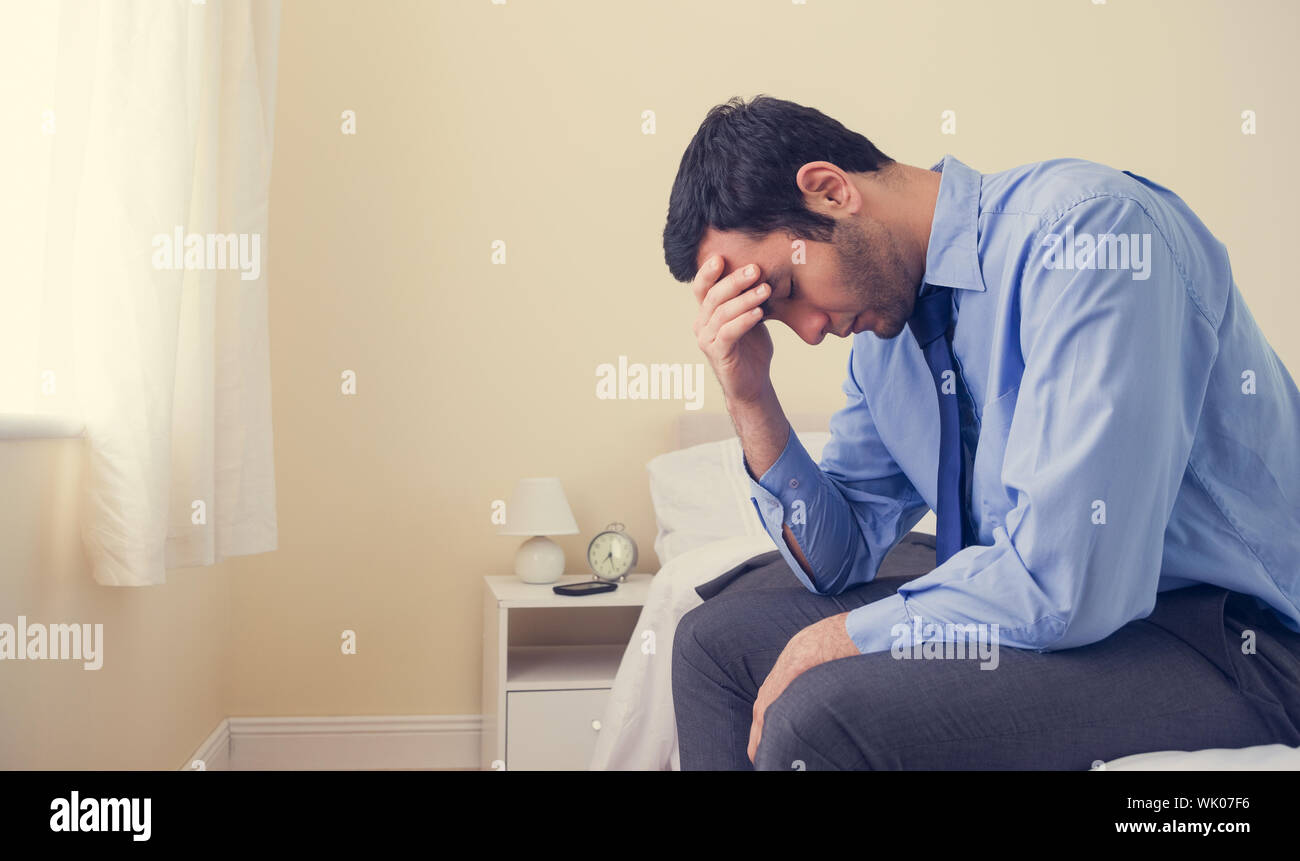 Premuto uomo seduto in testa le mani sul suo letto Foto Stock