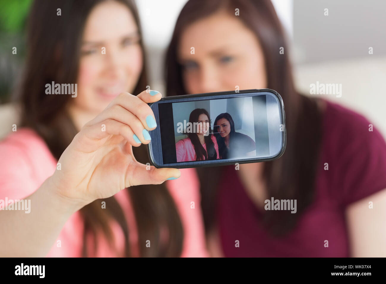 Due ragazze sorridenti seduto su un divano di scattare una foto di se stessi con un telefono cellulare Foto Stock