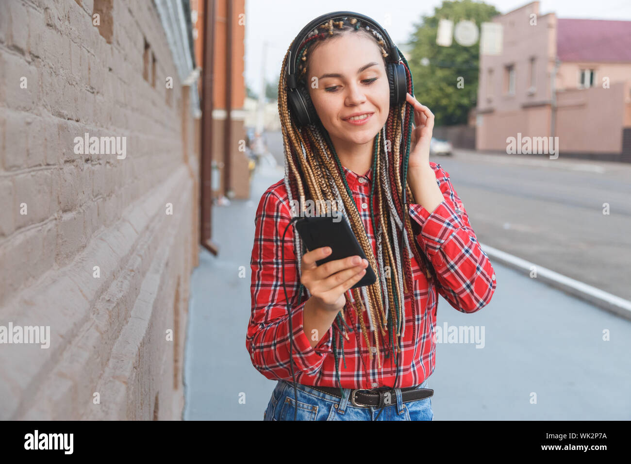 Giovane donna con colorato pigtail ascoltando la musica nelle cuffie sulla strada Foto Stock
