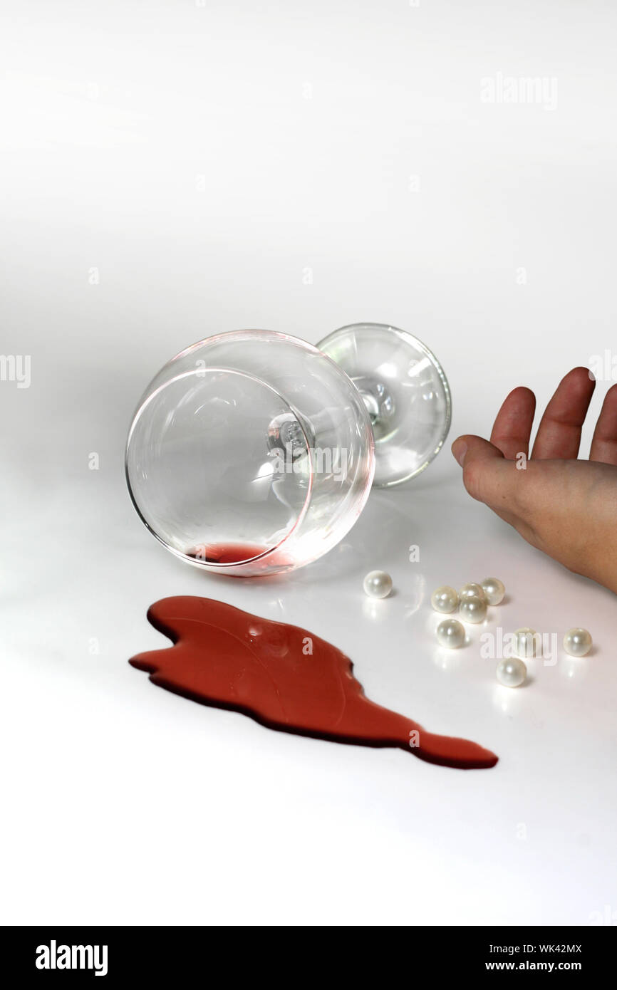 Un bicchiere di vino caduto sul pavimento con una mano morta accanto ad esso Foto Stock