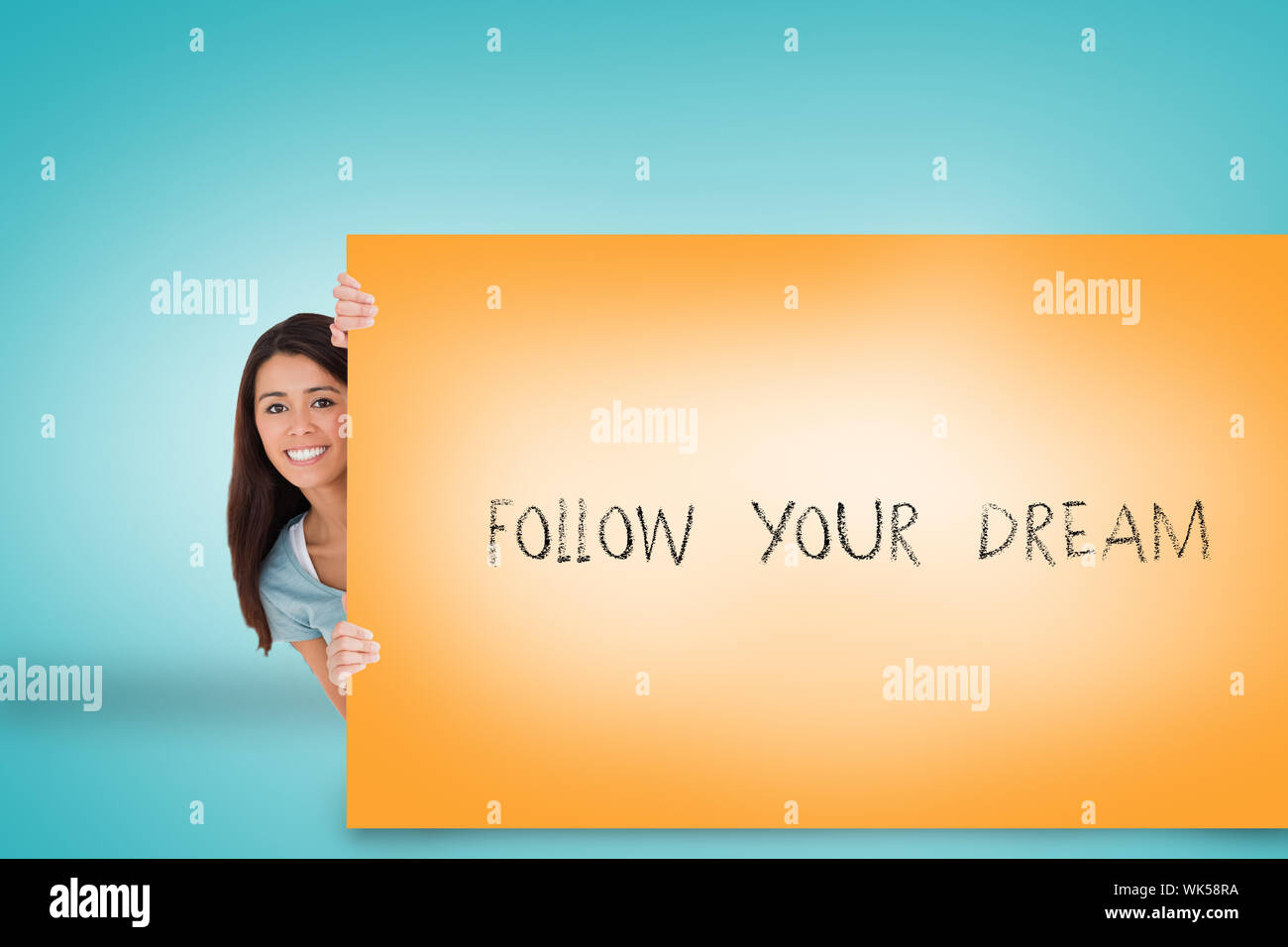 Bella bruna che mostra scheda con seguire il tuo sogno contro sfondo blu Foto Stock