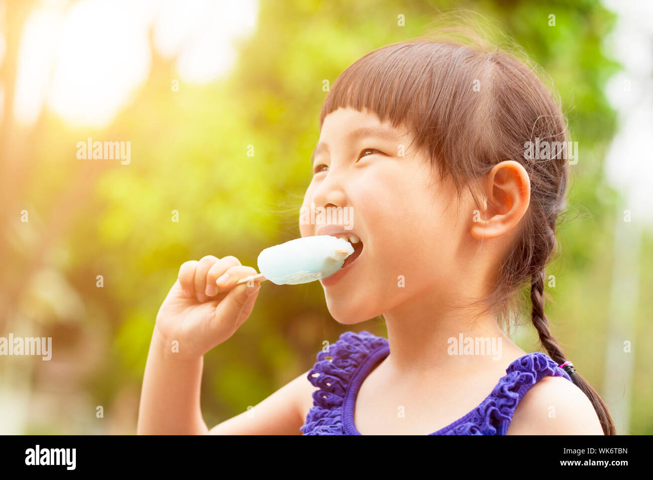 Felice bambina mangiare ghiaccioli in estate con il tramonto del sole Foto Stock