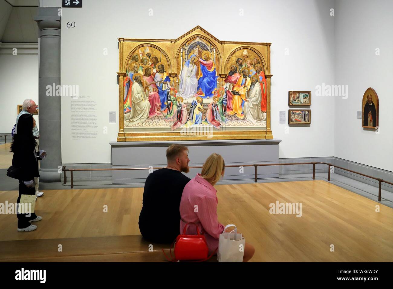 Una giovane coppia seduta in un area espositiva con un dipinto di Lorenzo Monaco nel fondo alla National Gallery, Trafalgar Square, London, Regno Unito Foto Stock
