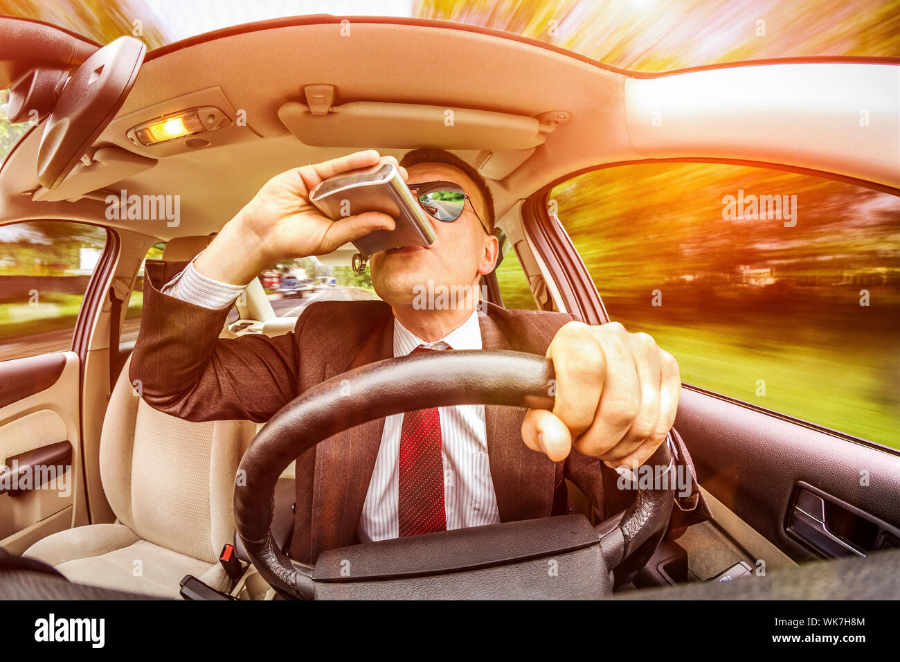 Uomo ubriaco in una tuta e occhiali da sole la guida su una strada in automobile veicolo. Foto Stock