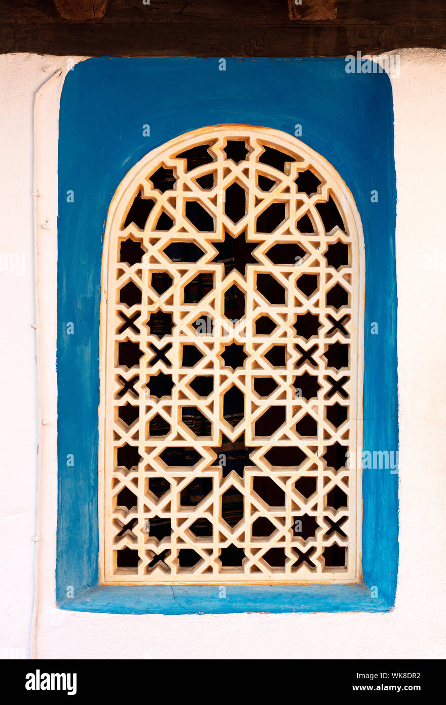 Finestra con un blu cornice dipinta su un muro bianco, il traliccio è bianco in ceramica con ornamento arabo Foto Stock