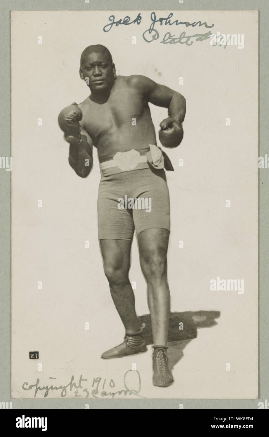 Jack Johnson, ritratto a figura intera, in piedi rivolto verso la parte anteriore, indossare pantaloncini boxe e guantoni da pugilato Foto Stock