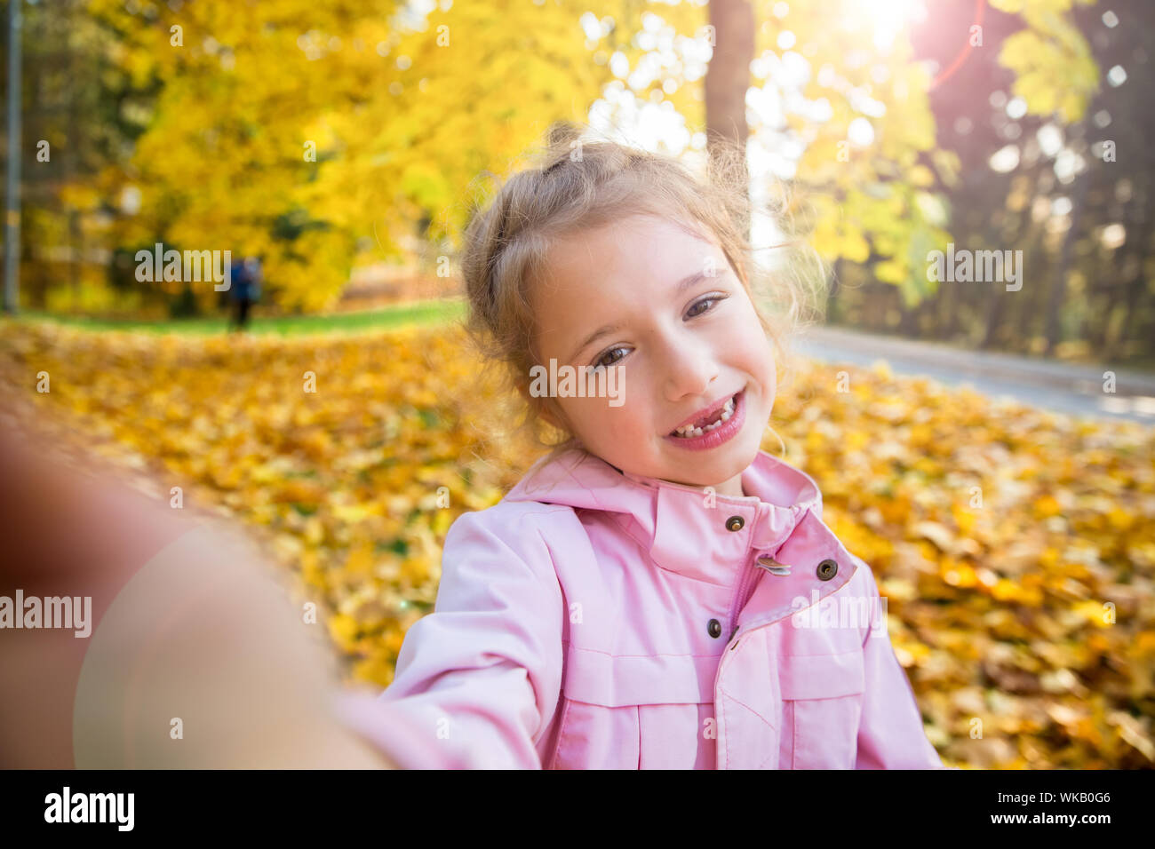 Carino bambina con denti mancanti tenendo selfie. Bambino felice ridendo e sorridendo. Sunny autunno foresta, fascio di sun. Foto Stock
