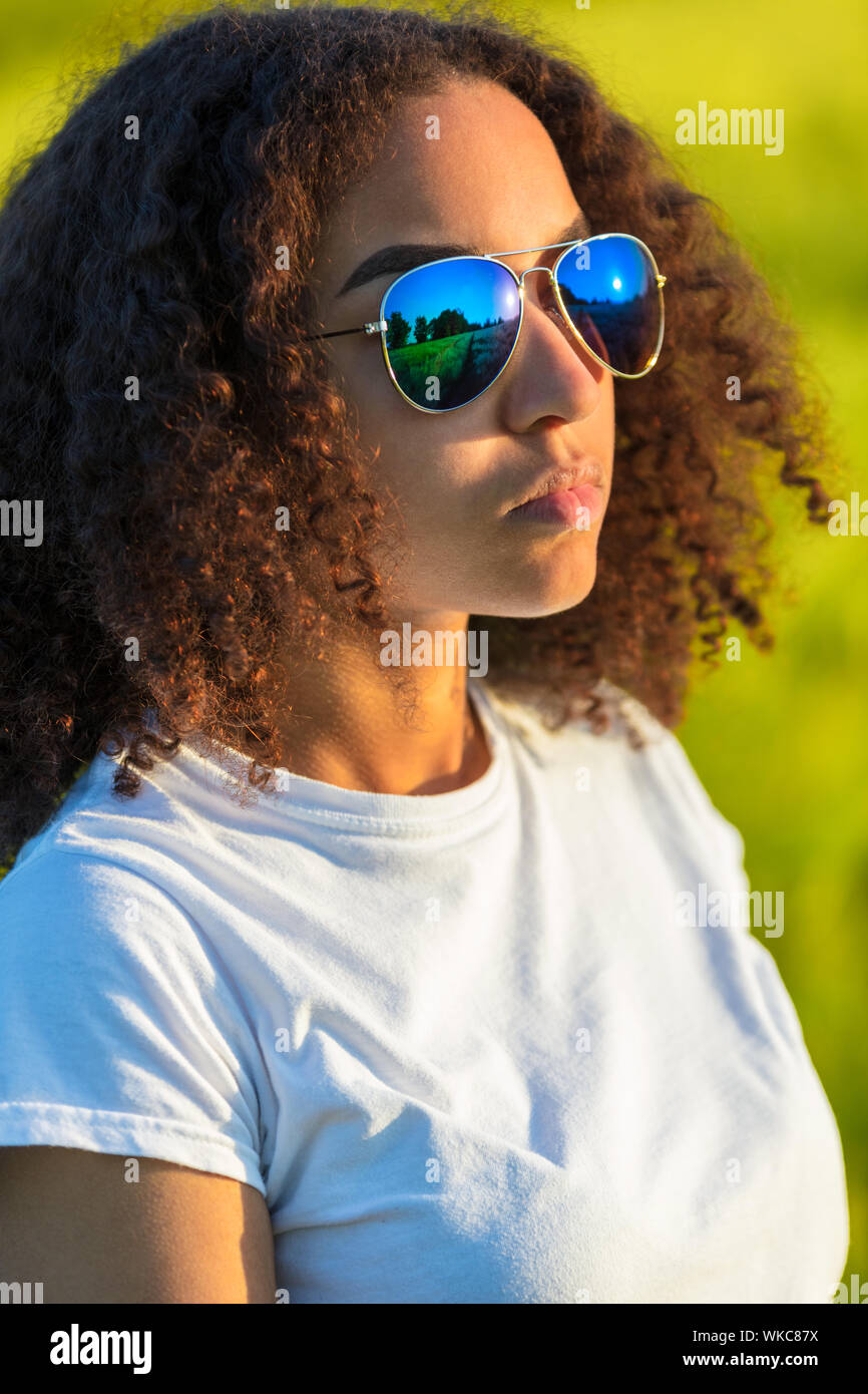 Bella e felice di razza mista biracial americano africano ragazza adolescente figlio giovane donna nel tramonto del sole indossando occhiali da sole Foto Stock