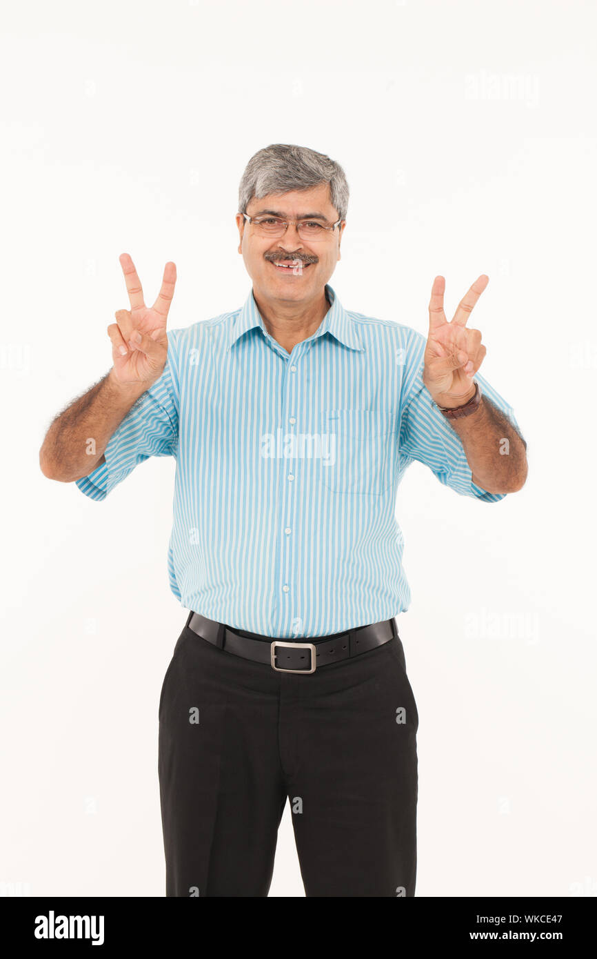 Uomo d'affari che mostra il segno V e sorridente Foto Stock