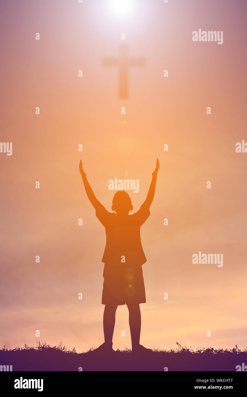 Digital immagine composita del ragazzo con le braccia sollevate in piedi al di sotto di Croce contro il cielo nuvoloso durante il tramonto Foto Stock