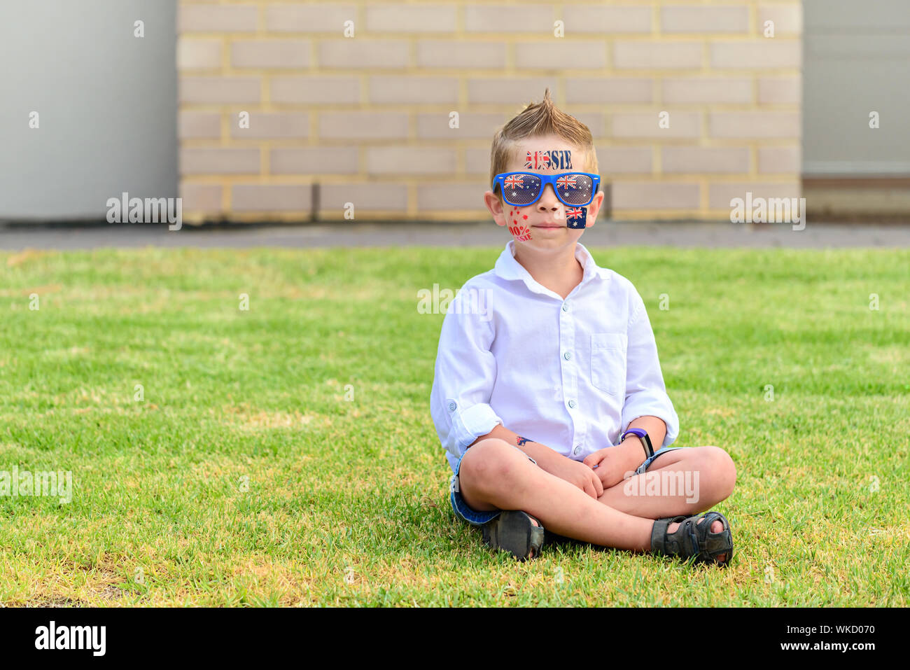 Sorridente ragazzo Australiano con occhiali da sole seduto su un prato durante l'Australia Day celebrazione Foto Stock