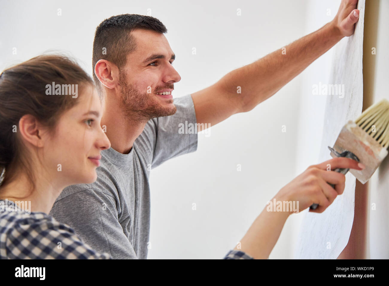 Coppia giovane wallpapering con uno sfondo sulla parete mentre il rinnovamento di casa o appartamento Foto Stock