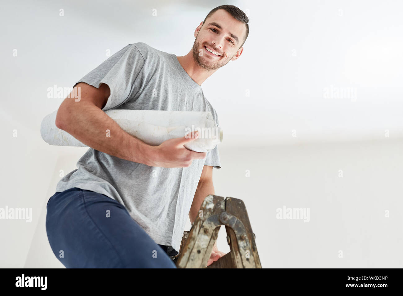 Giovane uomo con uno sfondo su una scaletta durante la tappezzeria e il rinnovamento nella nuova casa Foto Stock