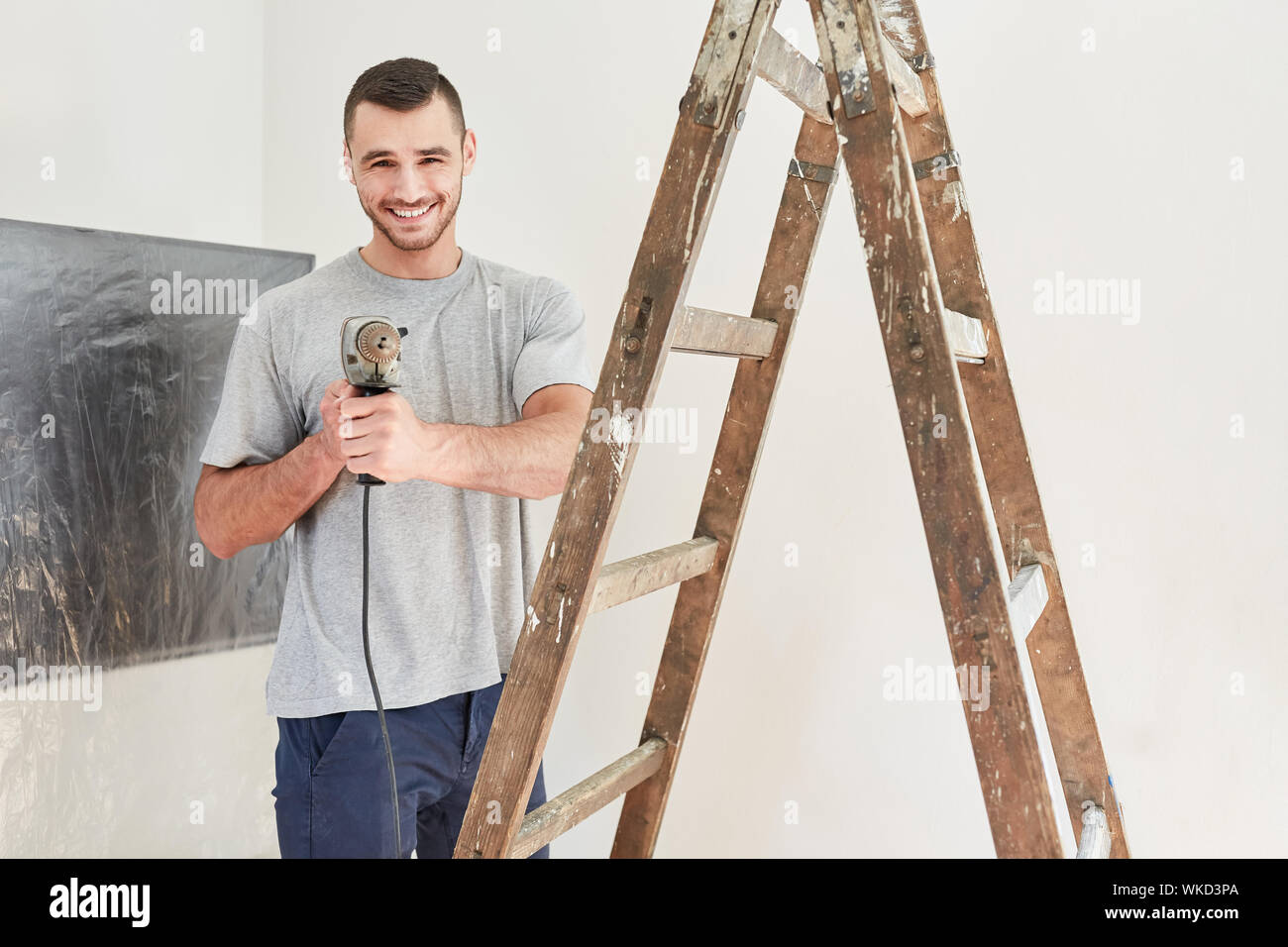 Felice giovane come un tuttofare con trapano è guardare avanti per la ristrutturazione Foto Stock