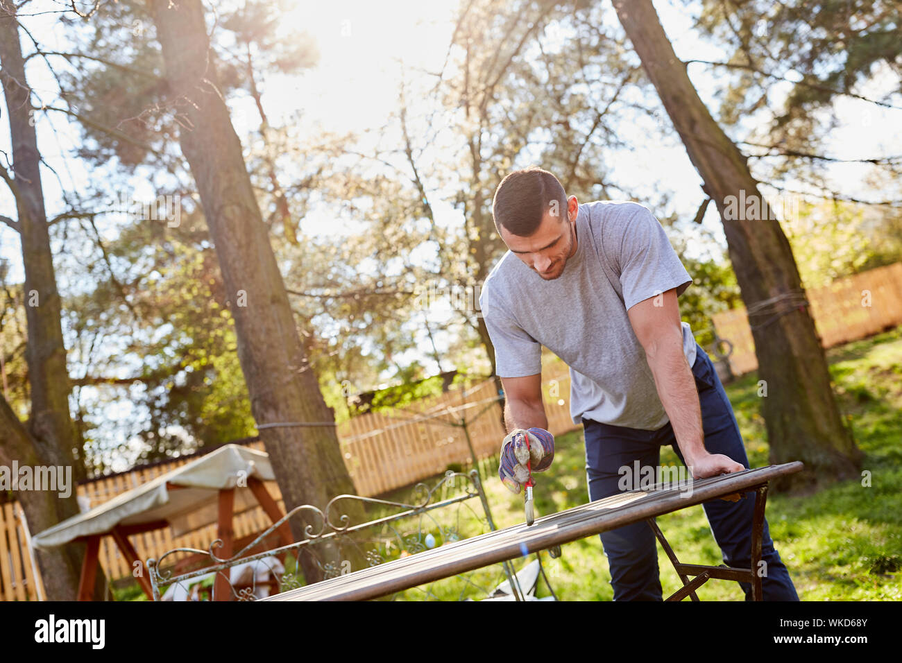 Giovane uomo a mobili da giardino di primer e di vernice come home opere di miglioramento in estate Foto Stock