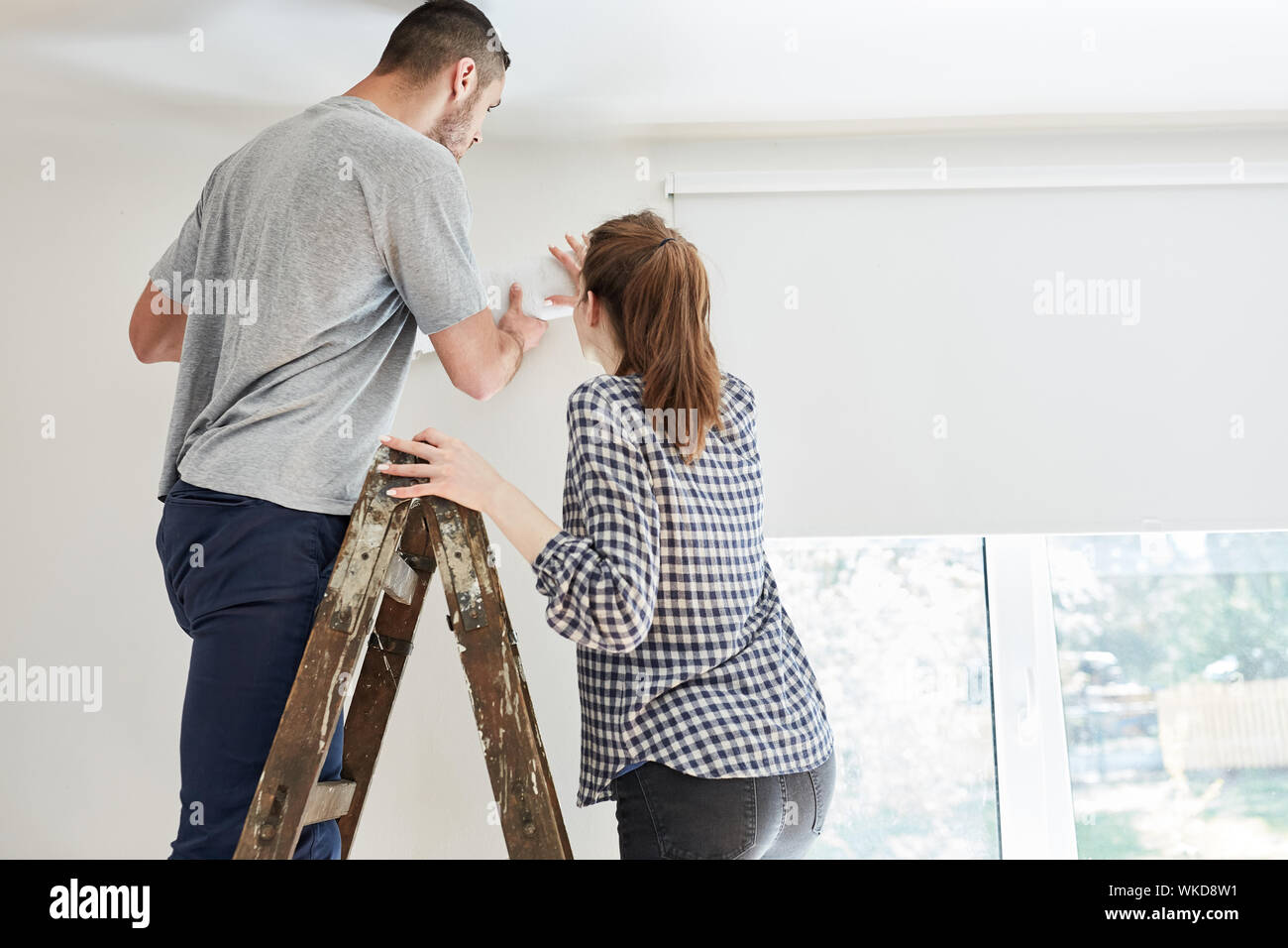 Giovane wallpapering con uno sfondo sulla parete mentre il rinnovamento di una casa Foto Stock