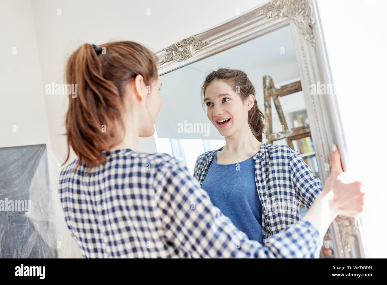 Sorridente giovane donna in casa o appartamento impostazione pende un mirror Foto Stock