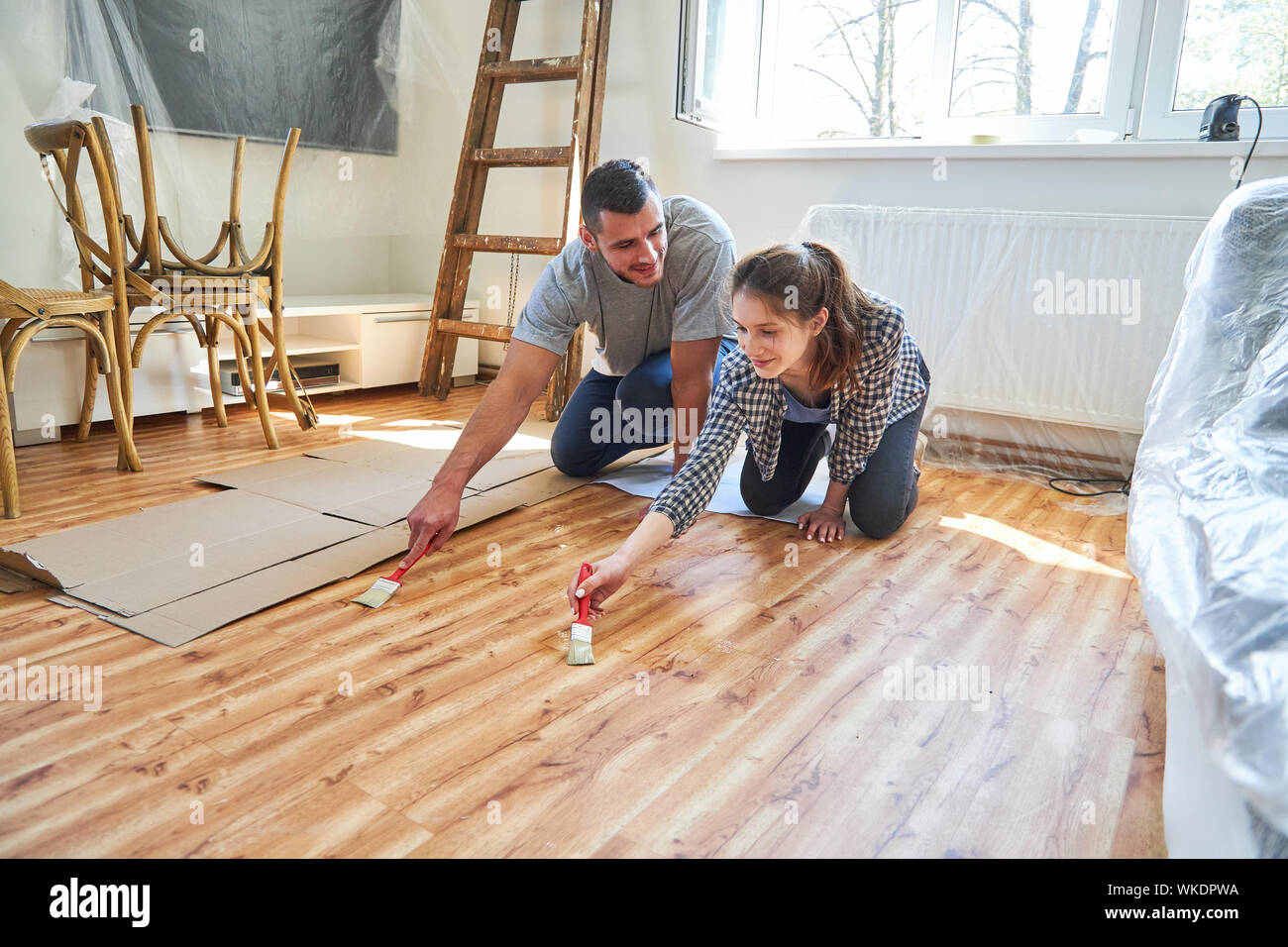 Coppia giovane al pavimento in parquet vernice nel nuovo appartamento come un miglioramento di casa il lavoro Foto Stock