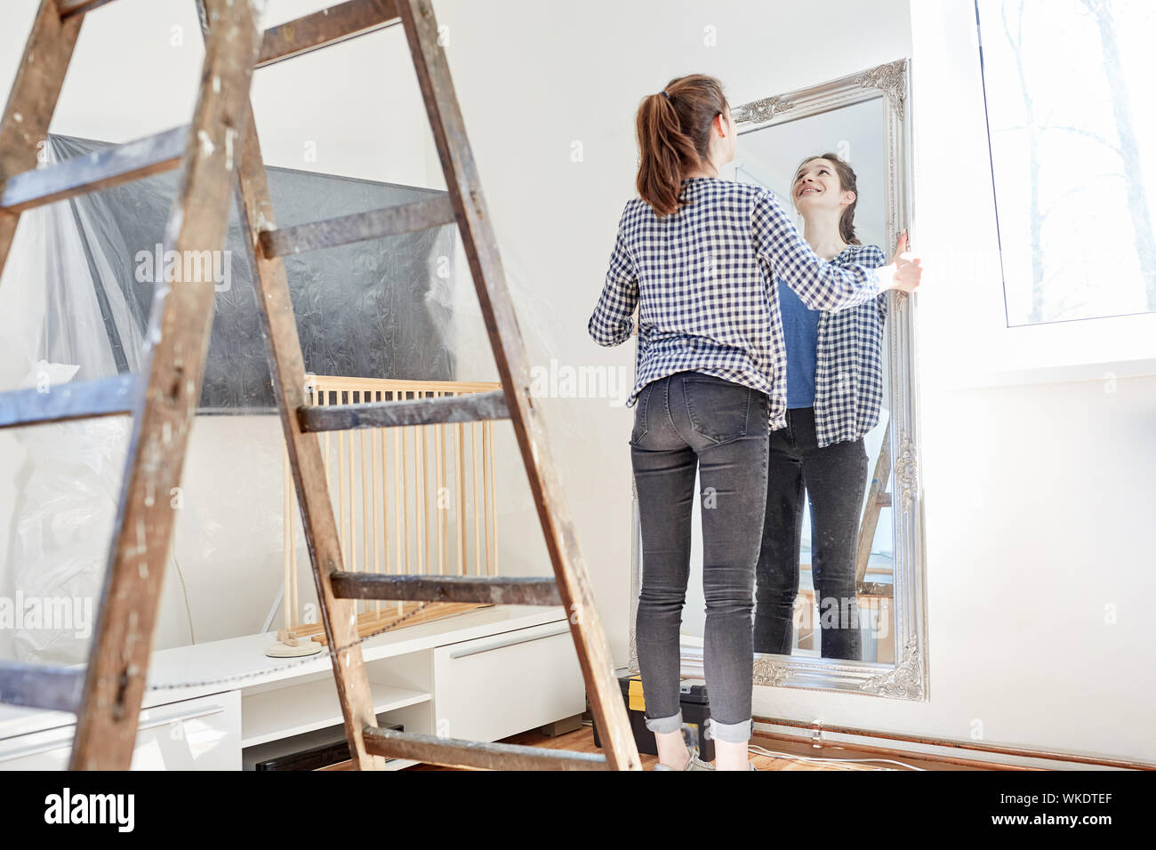 Giovane donna costruisce un nuovo appartamento e pende un grande specchio sulla parete Foto Stock