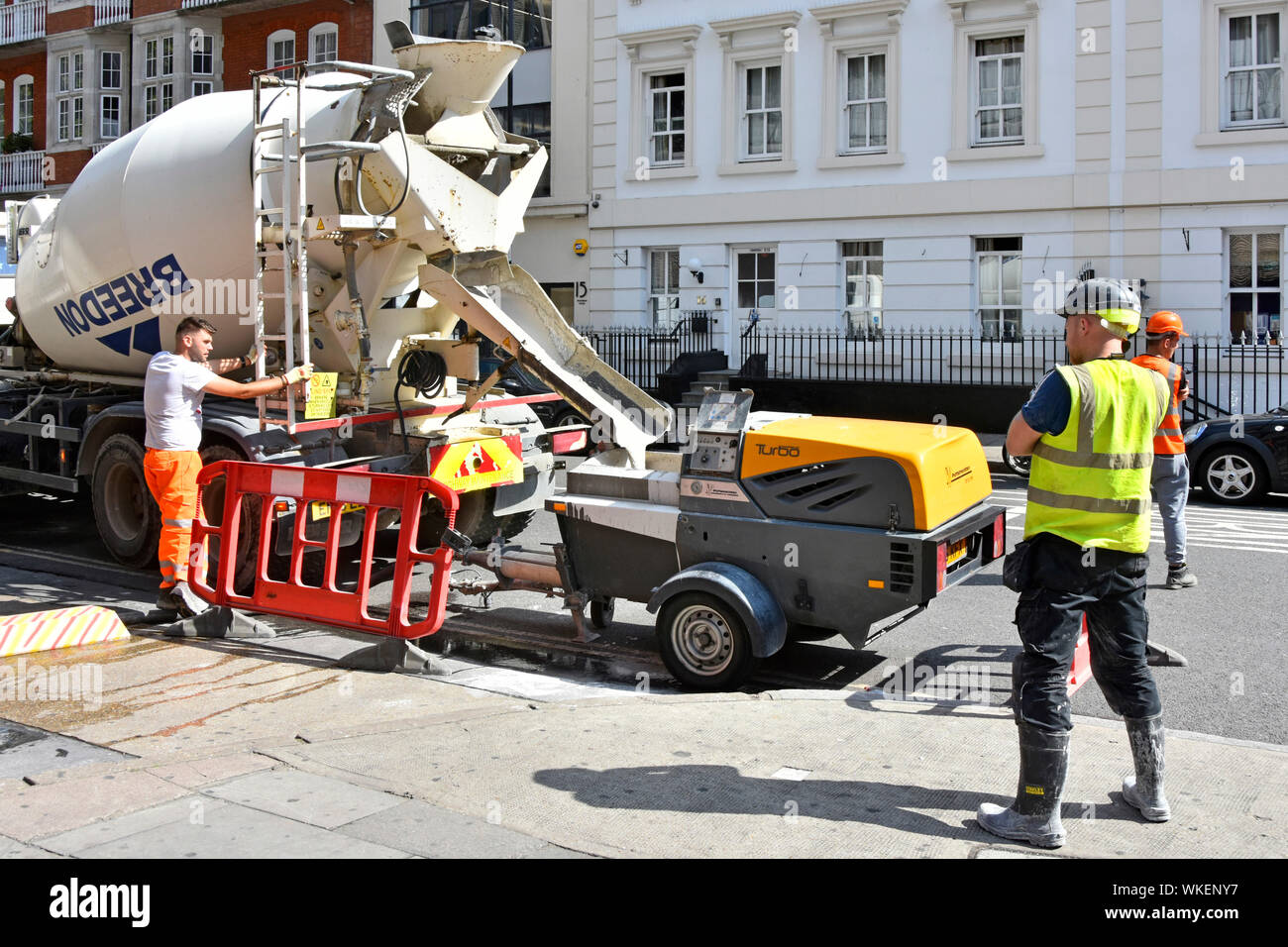 Operai & pre cemento mescolato Pompa per sottofondi di erogazione del calcestruzzo carrello un camion a rimorchio di piccole dimensioni il pompaggio tramite un tubo flessibile per la costruzione dell'edificio sito London REGNO UNITO Foto Stock