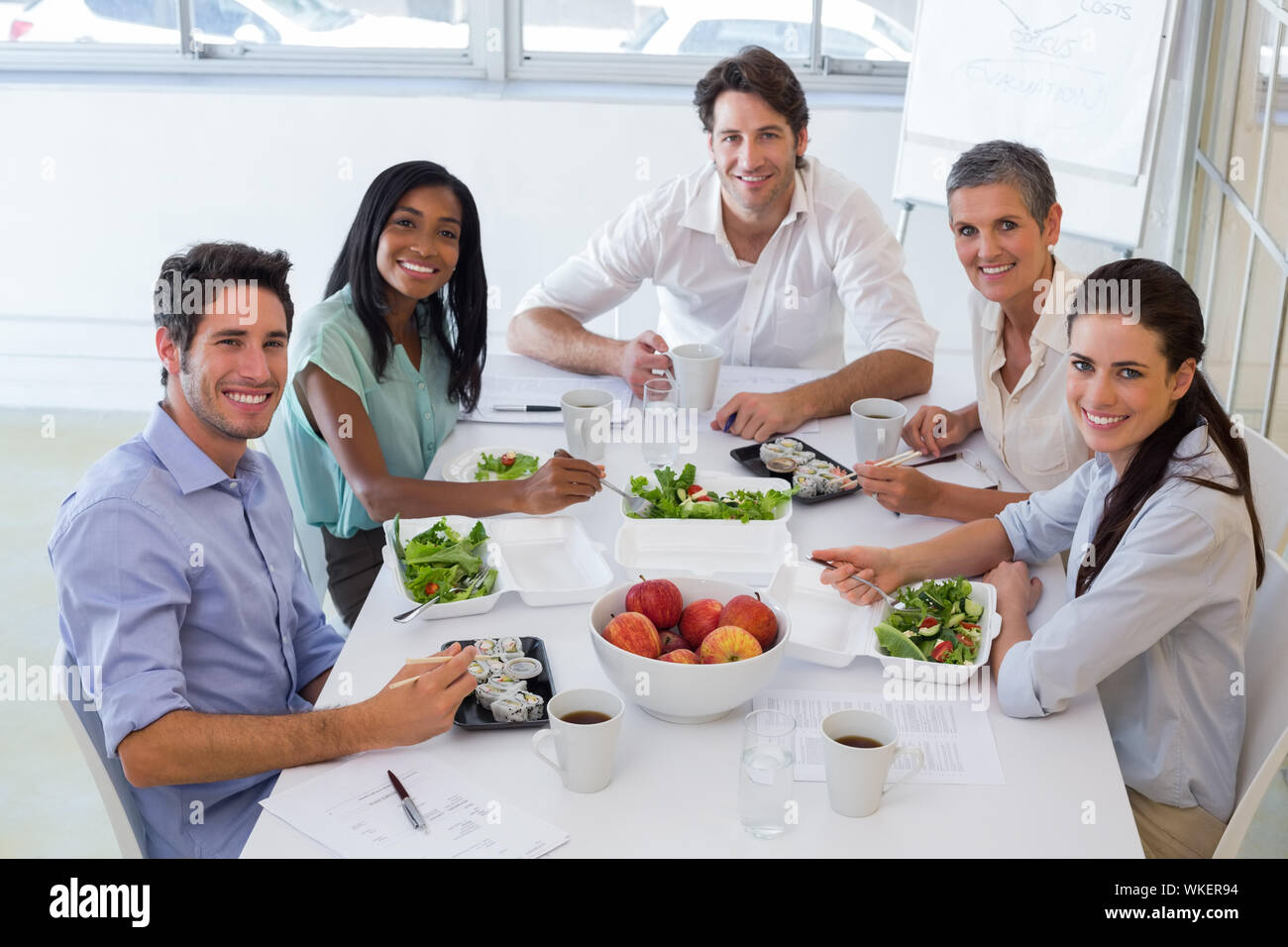 Lavoratori sorriso alla telecamera mentre mangiare sano il pranzo in ufficio Foto Stock