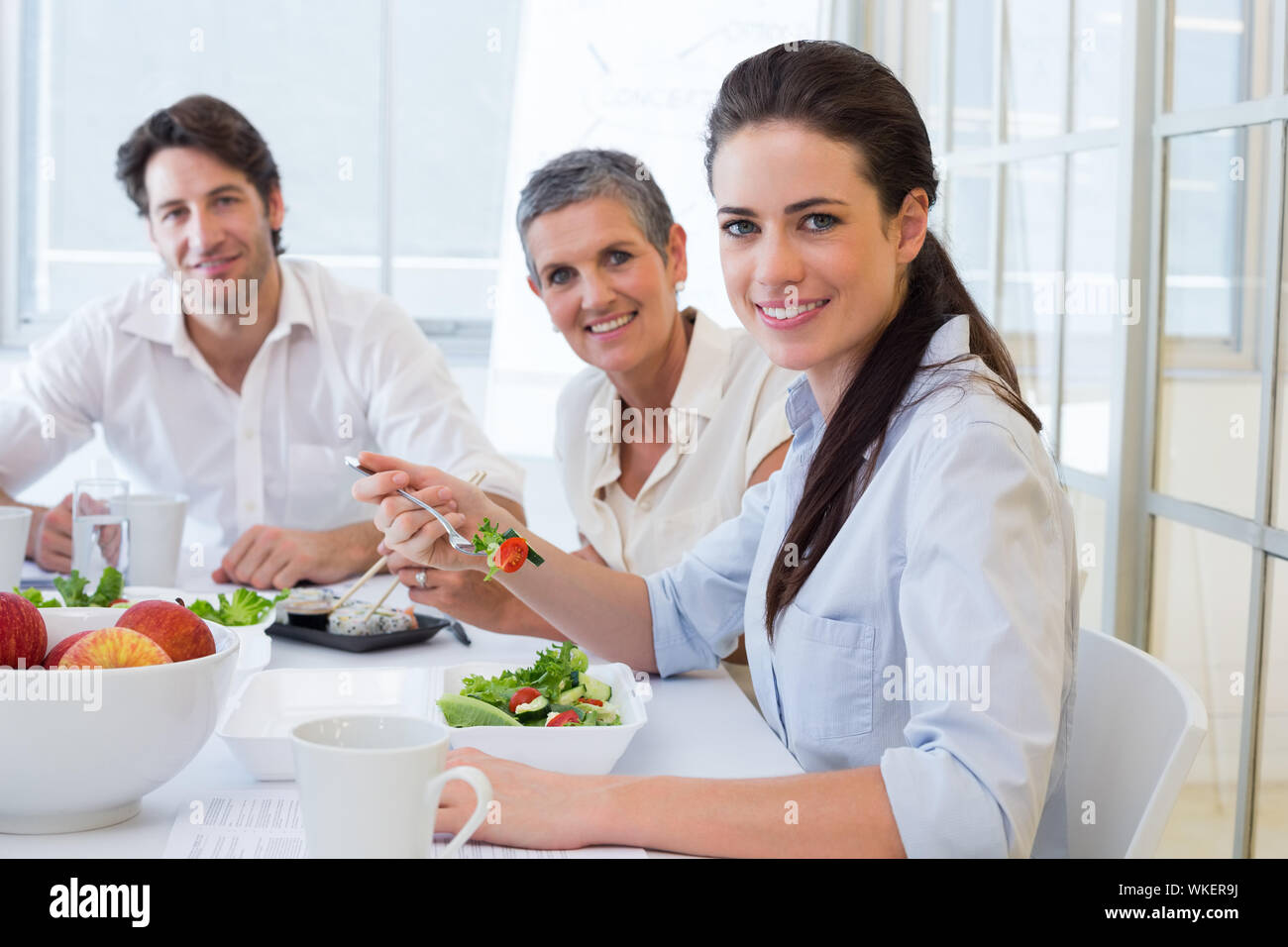 I lavoratori di mangiare il pranzo il sorriso a telecamera in ufficio Foto Stock