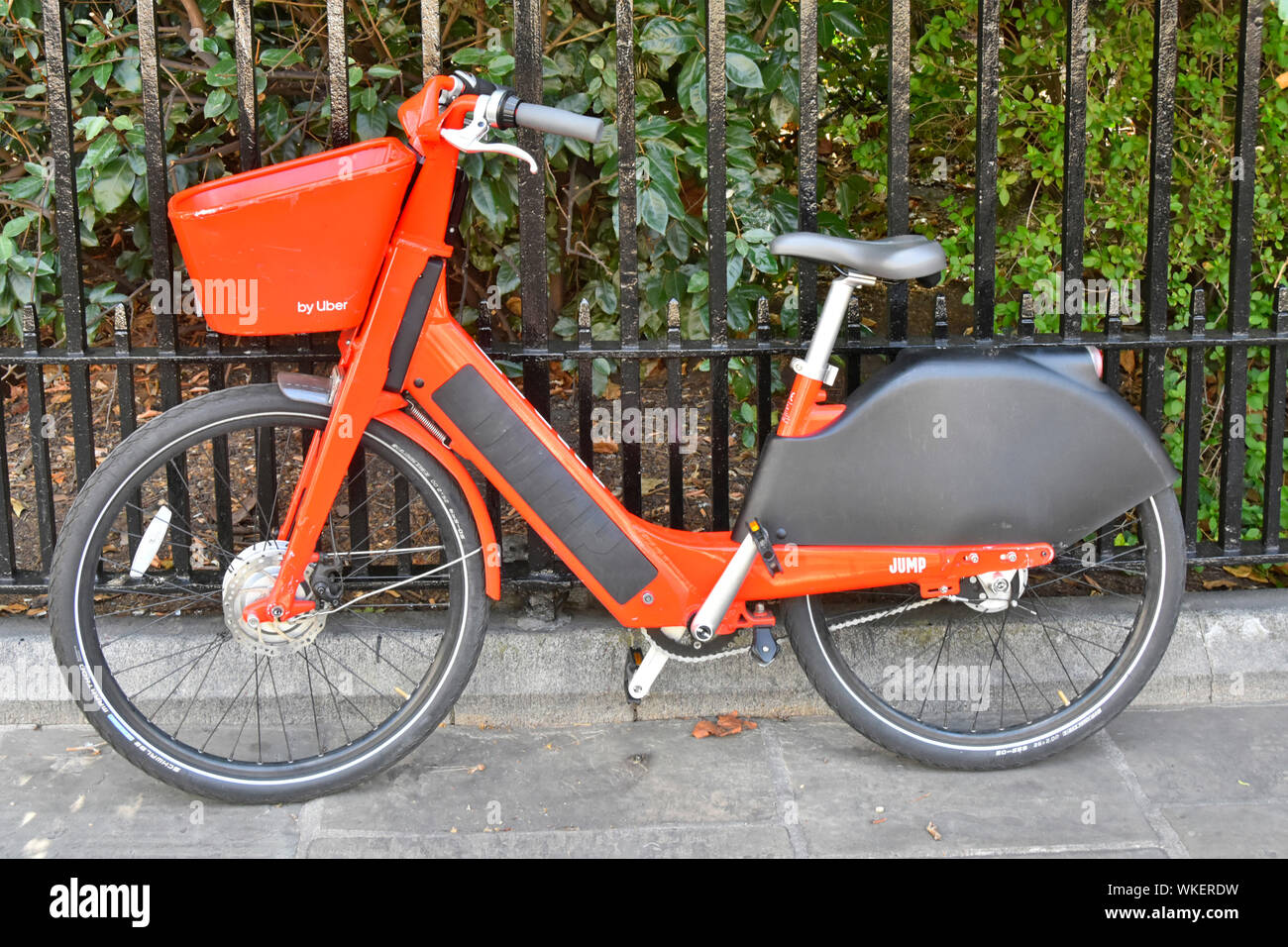 Colore arancione Jump affitto Noleggio bici da Uber elettrici alimentati a batteria app GPS tracker pedale elettrico assistere bicicletta parcheggiato a fianco di ringhiere Londra Inghilterra REGNO UNITO Foto Stock